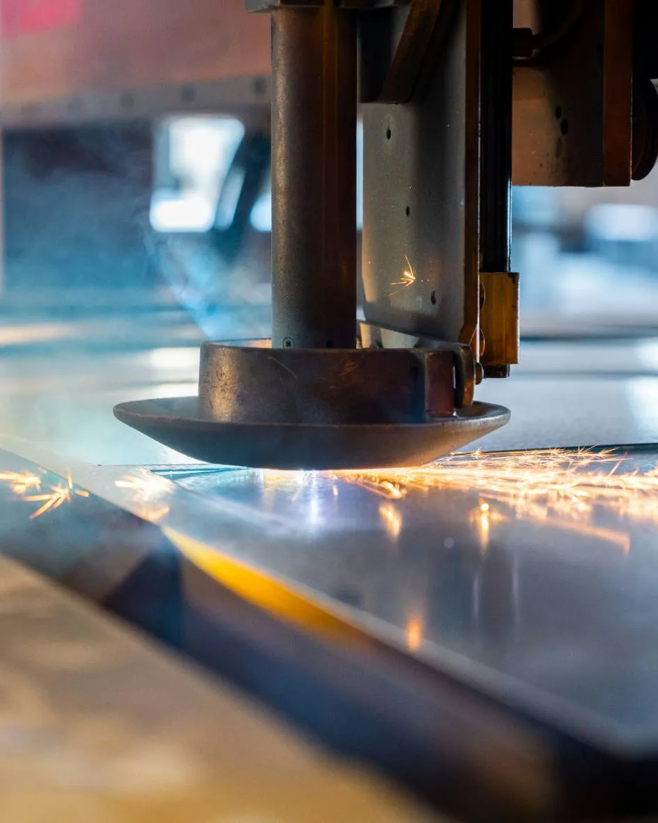 Industrial laser cutting head tracing a sheet of steel with sparks along the cut, advanced materials and manufacturing.