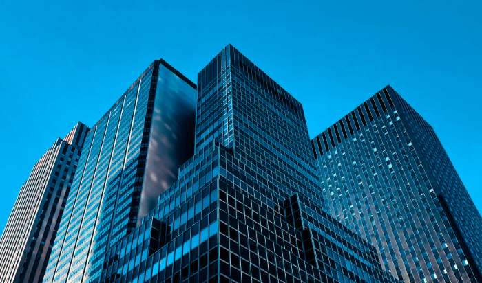 Glass corporate office towers seen from below against a clear blue sky, representing enterprise R&D and innovation teams.